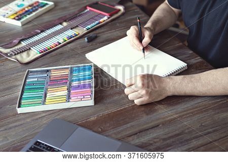 Man Painting With Color Pencil And Pastel Crayon Chalks On Paper On Wooden Table