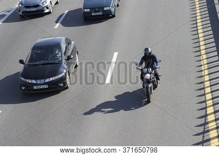 A Motorcyclist In A Helmet Rides A Small Motorcycle Along A Wide Freeway, A Ring Road Among Passenge