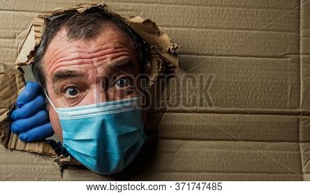 Surprised scared adult male in medical mask and protective latex gloves looks through a hole in cardboard