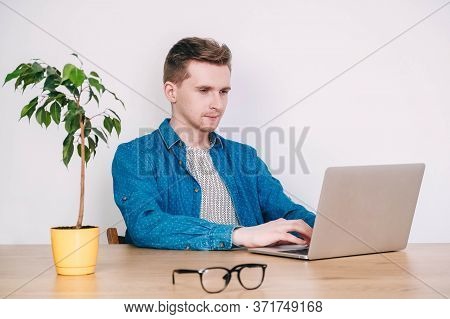 Young Man In Shirt And Glasses Working On Laptop Computer Sitting At The Table On A White Background