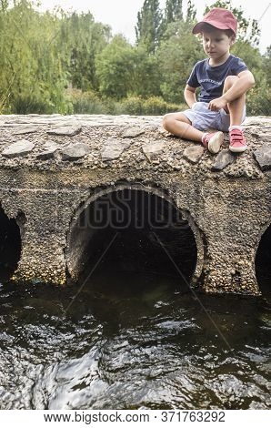 Little Boy Sitting Over Bridge Observing How The Water Flows. Discovering Nature For Children Concep