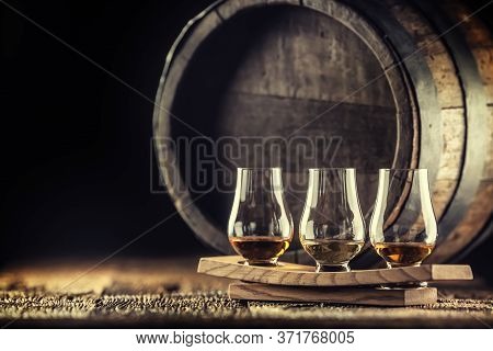 Glencairn Whiskey Tasting Cups On A Wooden Serving, With A Whisky Barrel In The Dark Background.