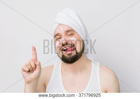 Funny Bearded Man With White Towel On His Head Showing His Finger With Face Cream On It, Smears A Cr