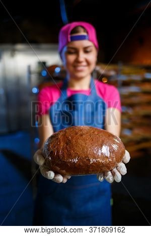 A Baker Girl Takes Hot Bread In A Bakery Against The Background Of Shelving With Bread. Industrial P