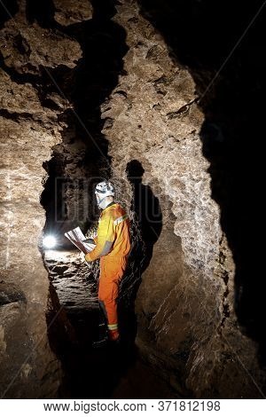 Man Walking And Exploring Dark Cave With Light Headlamp And Map In His Hand Underground.
