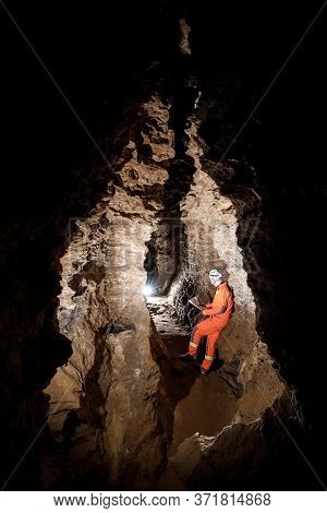Man Walking And Exploring Dark Cave With Light Headlamp And Map In His Hand Underground.