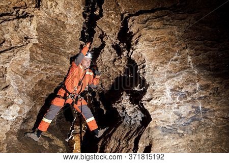 Speleologist Descend By The Rope In The Deep Vertical Cave Tunnel.