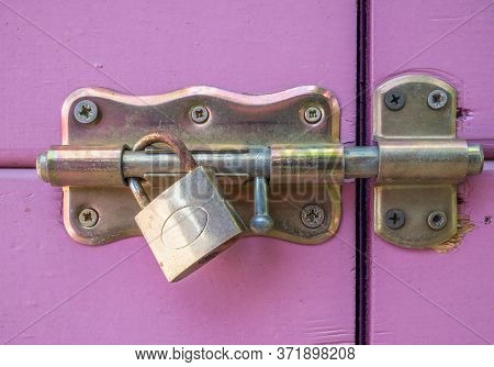Close Up With A Locked Purple Door. Door Latch With A Rusty Golden Lock..