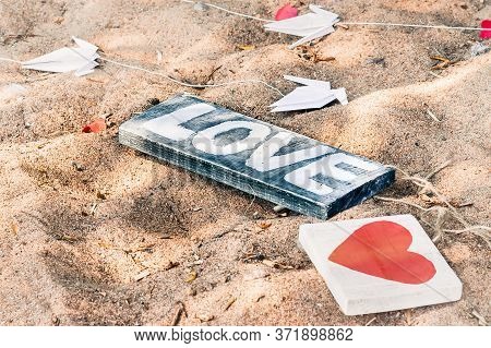 Wooden Sign Love, Heart And Paper Cranes Lie On The Sandy Beach. Wedding Decoration On The Beach In 