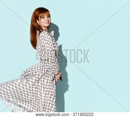 Young Pretty Smiling Red-haired Woman In Elegant Flying Light Dress Standing Side To Us And Looking 