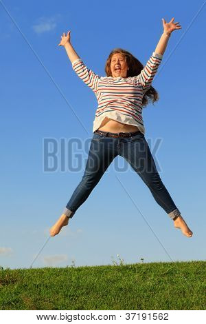 Ung pige i jeans hopper og skriger på grønne græs på baggrund af blå himmel.