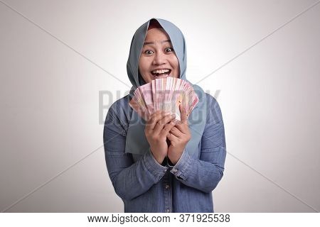 Portrait Of Indonesian Muslim Woman Holding Rupiah Money, Smiling Laughing Winning Gesture