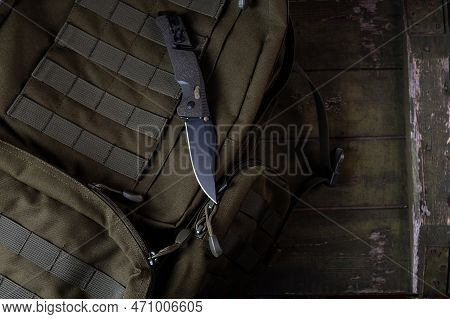 Folding Sharp Army Knife On A Military Backpack. Knife With Clip And Safety. Backpack With Molle Rib