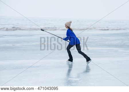 A Caucasian Woman Is Skating On A Frozen Lake Holding A Selfie Stick In Her Hands. The Figure Skater