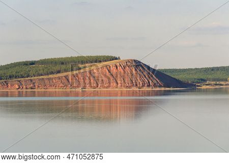 Lake With Clouds In The Sky, Red Hill With Forests On Background. Hill Symmetric Reflection In The W