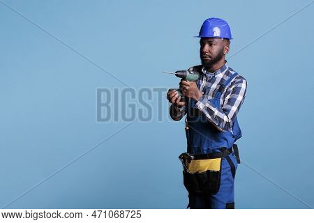 Concentrated African American Builder Holding Cordless Drill Against Blue Background. Professional M