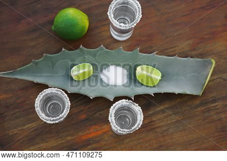 Mexican Tequila Shots, Salt, Lime And Green Leaf On Wooden Table, Flat Lay. Drink Made Of Agava