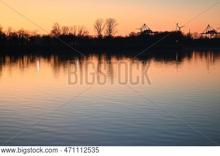 Evening Mood Besides A River Against A Containerport And Sunset