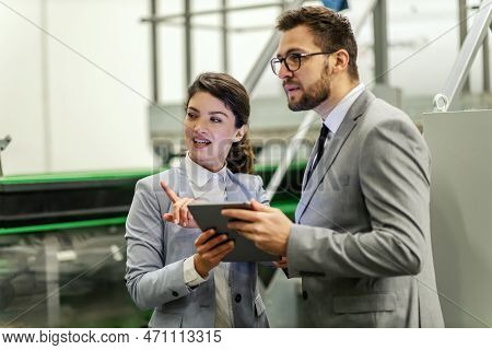 Business People In A Working Environment Inside A Factory. A Man And A Woman In An Elegant Suit Insp