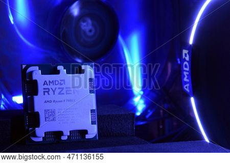 Close-up Of An Amd Ryzen 9 7900X Processor, Against The Backdrop Of Coolers With Light.