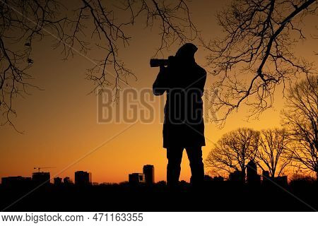 A Photographer Stands Beneath The Barren Oak Branches As He Takes In Dawn't Twilight Of The City. Vi