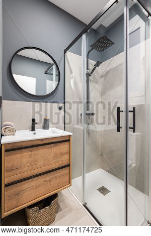 Bathroom With A Washbasin On A Floating Vanity. On A Gray Wall Is A Round Mirror In A Black Metal Fr