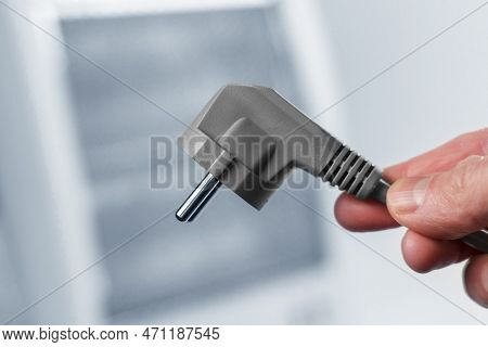 Electric Plug In Hand On Cold Home Halogen Heater Background In Blur. Disconnected Heating Appliance