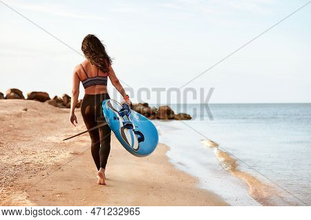 Woman Surfer With Surfboard Going To Surf At Seaside. Girl Holding Surfboard O And Goes To The Ocean