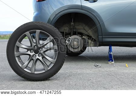 Car Lifted By Scissor Jack And New Wheel On Roadside. Tire Puncture