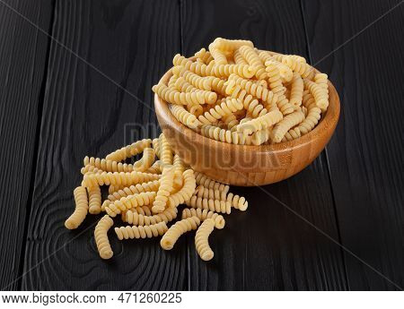 Dry Fusilli Pasta In Wooden Bowl On Black Wooden Background