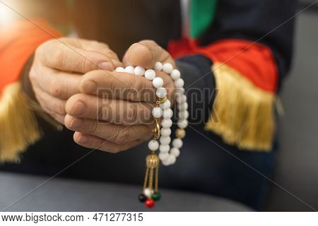 An Elderly Man Prays With A Rosary And The Flag Of The United Arab Emirates