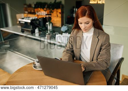 Beautiful Businesswoman With Ginger Hair Typing On A Laptop While Sitting At A Table In A Coffee Sho