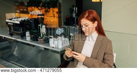 Beautiful Female With Ginger Hair Holding A Mobile Phone. Businesswoman In Formal Wear Typing On A M