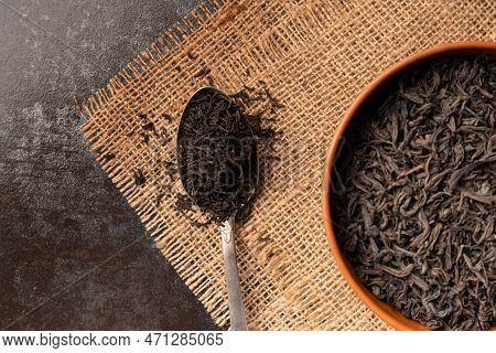 Dry Black Tea Leaves In A Clay Bowl And A Vintage Spoon On A Dark Wooden Background Top View. Large-