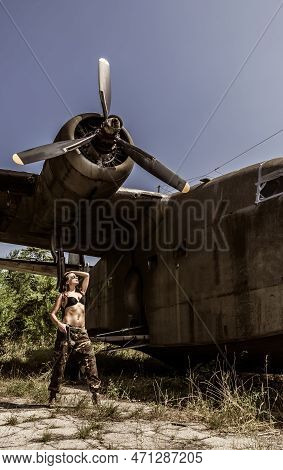 Portrait Of A Young Girl With Mimetic Military Dress Near The Old Abandoned Broken Plane. Concept Mi