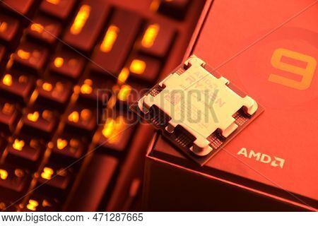 A Close-up Of An Amd Ryzen 9 7900X Processor In A Packaging Box With Backlit Keyboards In The Backgr