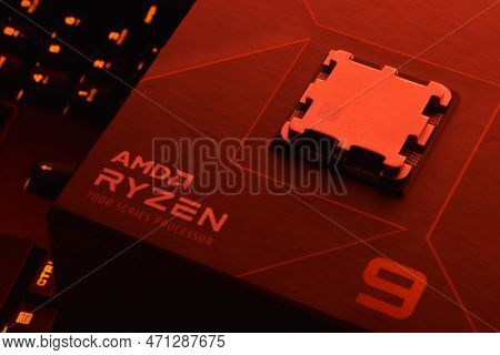 A Close-up Of An Amd Ryzen 9 7900X Processor In A Packaging Box With Backlit Keyboards In The Backgr
