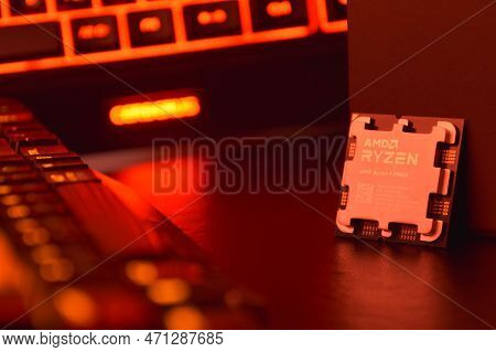A Close-up Of An Amd Ryzen 9 7900X Processor In A Packaging Box With Backlit Keyboards In The Backgr