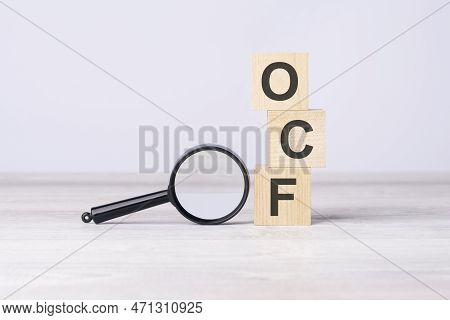 Concept Operating Cash Flow Or Ocf. Text On Wooden Cubes Under A Magnifying Glass.