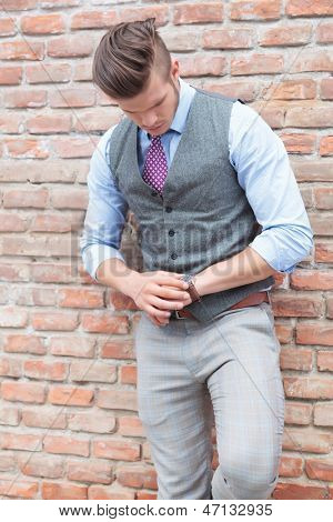 casual ung mand stående ved en mur og ser på sit ur, kontrollere tid