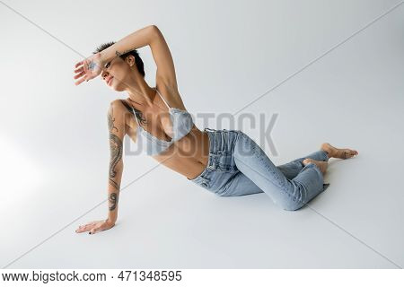 Full Length Of Sexy Barefoot Woman In Silk Bralette And Blue Jeans Obscuring Face With Hand While Po