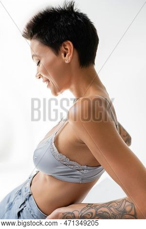 Side View Of Brunette Short Haired Woman In Satin Bralette Smiling On Grey Background.