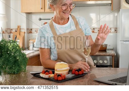 Happy Senior Woman In The Home Kitchen After Baking Her Homemade Plumcake In Video Chat By Laptop Ho
