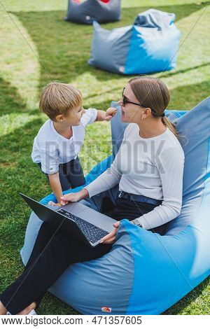 A Mother With Her Son On A Green Lawn, A Mother On Maternity Leave Is Working On A Laptop In The Par