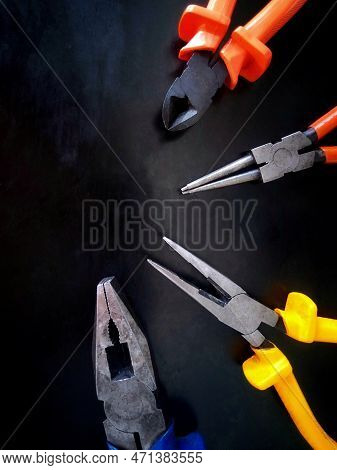 Different Pliers Used In Mechanical Workshop Over The Black Worktable.
