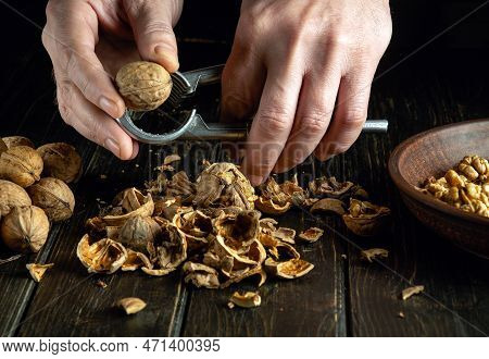 Close-up Of A Man's Hands With A Nutcracker On The Kitchen Table. Peeling Nuts With A Nutcracker By 