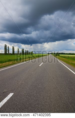 Empty Highway, Paved Road Through The Fields. Dramatic Sky, Rain On The Horizon In The Distance. The