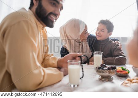 Positive African American Mother In Hijab Hugging Son Near Family And Suhur Breakfast At Home.