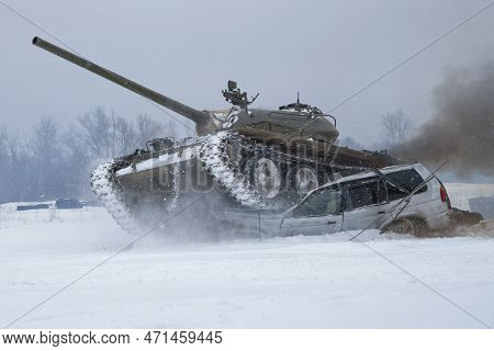 Krasnoye Selo, Russia - February 19, 2023: A Soviet Tank T-54 Crushes A Old Passenger Car In A Snowy