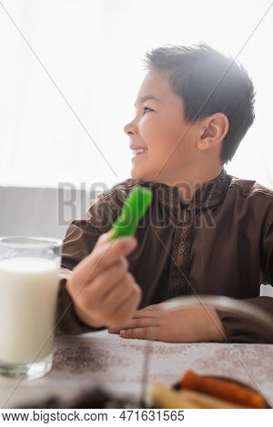 Side View Of Cheerful Muslim Boy Holding Blurred Cevizli Sucuk During Suhur At Home.
